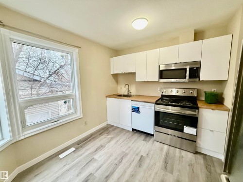 Kitchen featuring white cabinetry, wood-finish countertops, stainless steel appliances, and wood-finish flooring - 10905 74 Avenue, Edmonton, AB - Indoor Photo Showing Kitchen
