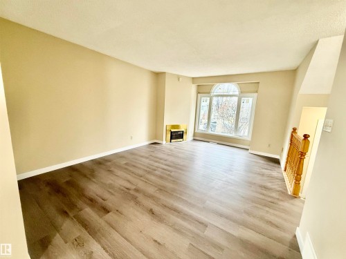 Spacious living area featuring light wood-finish flooring, neutral wall tones, and extensive natural light from a large arched window - 10905 74 Avenue, Edmonton, AB - Indoor