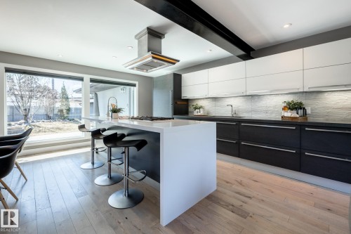 Modern kitchen featuring a waterfall island with a gas cooktop, light wood-finish flooring, two-tone cabinetry, and a textured tile backsplash - 4204 Aspen Drive E, Edmonton, AB - Indoor Photo Showing Kitchen With Upgraded Kitchen