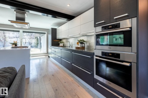 Kitchen featuring light wood-finish flooring, two-tone cabinetry with integrated stainless steel appliances, a center island with a sink and gooseneck faucet, and large windows - 4204 Aspen Drive E, Edmonton, AB - Indoor Photo Showing Kitchen