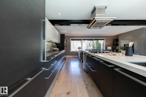 Modern kitchen featuring dark wood-finish cabinetry, a large center island with a light-colored countertop, and a stainless steel island range hood - 4204 Aspen Drive E, Edmonton, AB - Indoor Photo Showing Kitchen