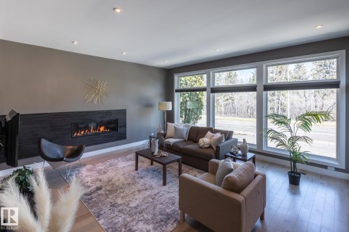 Linear fireplace with dark stone surround, recessed lighting, expansive windows with roller shades, and light wood-finish flooring - 4204 Aspen Drive E, Edmonton, AB - Indoor Photo Showing Living Room With Fireplace