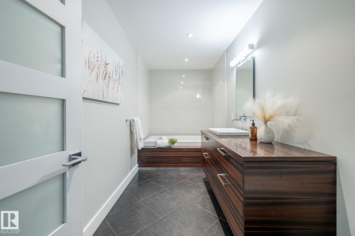 Modern bathroom featuring a wood-finish vanity with integrated sink, a built-in bathtub, and dark tile flooring - 4204 Aspen Drive E, Edmonton, AB - Indoor