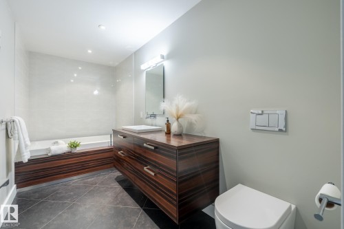 Modern bathroom featuring a dark wood-finish vanity with a vessel sink, a built-in bathtub with wood-finish paneling, white subway tile surround, and large format dark tile flooring - 4204 Aspen Drive E, Edmonton, AB - Indoor Photo Showing Bathroom