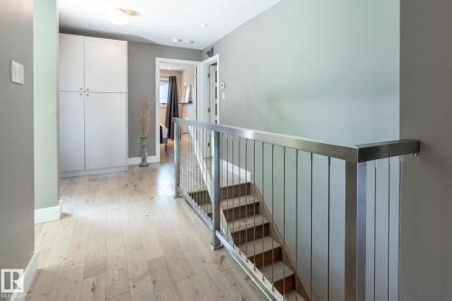 Hallway with light wood-finish flooring, built-in storage cabinetry, and a modern stair railing with stainless steel newel posts and balusters - 4204 Aspen Drive E, Edmonton, AB - Indoor Photo Showing Other Room