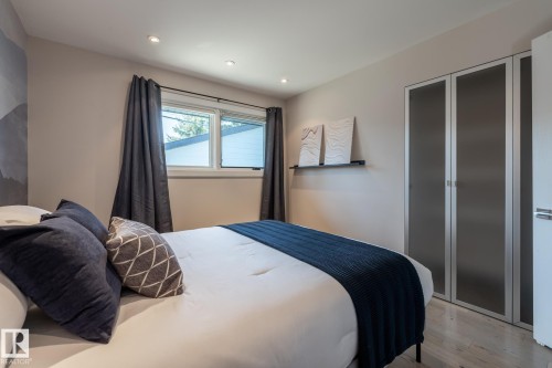 Recessed lighting illuminates this room, featuring a window with dark drapery panels, light wood-finish flooring, and a built-in closet with frosted glass doors - 4204 Aspen Drive E, Edmonton, AB - Indoor Photo Showing Bedroom