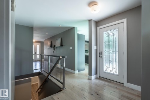 Entryway featuring a white door with decorative glass, wood-finish flooring, and a contemporary stair railing - 4204 Aspen Drive E, Edmonton, AB - Indoor Photo Showing Other Room