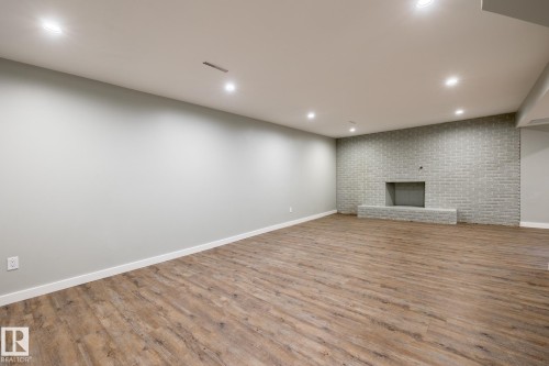 Spacious room featuring wood-finish flooring, a light gray painted wall, and a brick-finish accent wall with a fireplace - 4204 Aspen Drive E, Edmonton, AB - Indoor Photo Showing Other Room