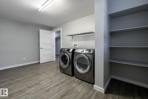 Dedicated laundry space featuring a front-loading washer and dryer, wood-finish flooring, built-in shelving, and a wall-mounted drying rack - 4204 Aspen Drive E, Edmonton, AB - Indoor Photo Showing Laundry Room