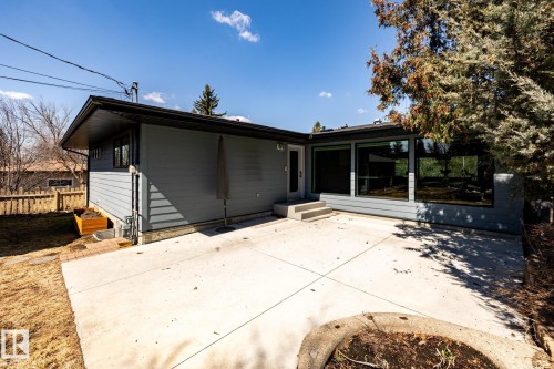 Expansive concrete patio with multiple large pane windows, a built-in circular planter, and an exterior door with concrete steps - 4204 Aspen Drive E, Edmonton, AB - Outdoor With Exterior