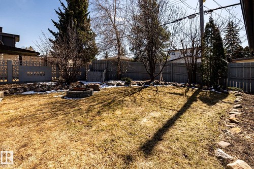Expansive backyard featuring a stone fire pit, wood fencing, a decorative concrete block wall, mature trees, and a stone-lined garden bed - 4204 Aspen Drive E, Edmonton, AB - Outdoor
