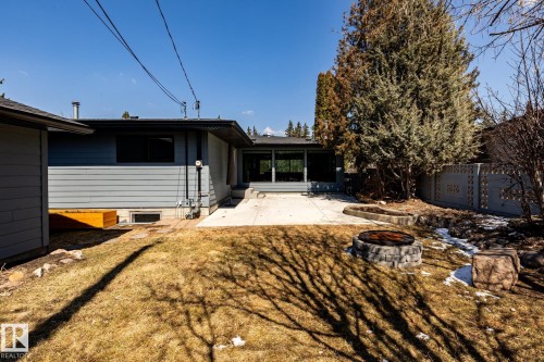 Expansive backyard featuring a concrete patio, a built-in stone fire pit, mature evergreen trees, and a decorative concrete block fence - 4204 Aspen Drive E, Edmonton, AB - Outdoor