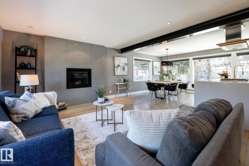 Open-concept living space featuring a modern fireplace insert, large windows, wood-finish flooring, recessed lighting, and a prominent structural beam - 4204 Aspen Drive E, Edmonton, AB - Indoor Photo Showing Living Room With Fireplace