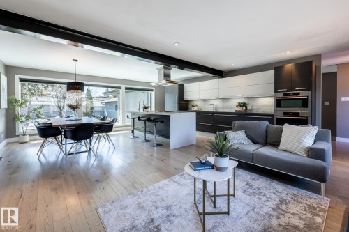 Open-concept living area featuring light wood-finish flooring, a contemporary kitchen with two-tone cabinetry, stainless steel appliances, and an island with bar seating - 4204 Aspen Drive E, Edmonton, AB - Indoor Photo Showing Living Room
