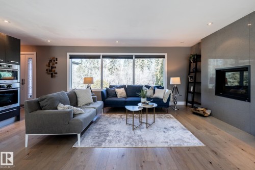 Expansive living area featuring light wood-finish flooring, a contemporary fireplace with a stone surround, and large windows providing abundant natural light - 4204 Aspen Drive E, Edmonton, AB - Indoor Photo Showing Living Room With Fireplace