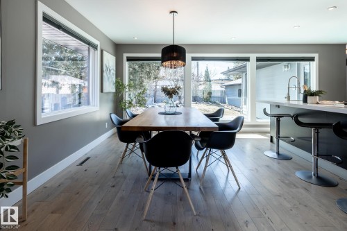 Open-concept dining area featuring light wood-finish flooring, a contemporary pendant light fixture, and large windows with white trim - 4204 Aspen Drive E, Edmonton, AB - Indoor Photo Showing Dining Room