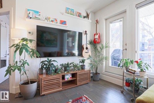 Spacious living area featuring dark wood-finish flooring, a white wall-mounted entertainment console, and two large windows - 202 10030 83 Avenue, Edmonton, AB - Indoor Photo Showing Other Room