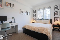 Bedroom featuring a large window with roller shade, neutral carpet flooring, white painted walls, and white baseboards - 