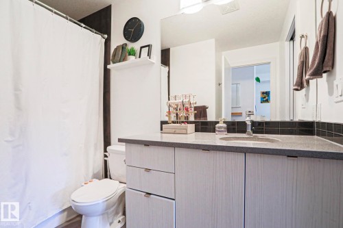 Bathroom featuring a light-toned wood-finish vanity with a built-in sink, dark speckled countertop, and a dark tile backsplash - 202 10030 83 Avenue, Edmonton, AB - Indoor Photo Showing Bathroom