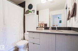 Bathroom featuring a light-toned wood-finish vanity with a built-in sink, dark speckled countertop, and a dark tile backsplash - 