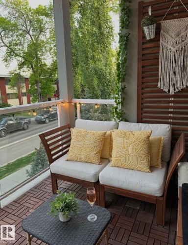 Balcony featuring wood-finish flooring, glass railing, and a slatted wood accent wall - 202 10030 83 Avenue, Edmonton, AB - Outdoor With Deck Patio Veranda With Exterior