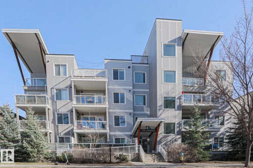 Modern multifamily building featuring a grey and light blue facade, multiple balconies with glass railings, a prominent entrance canopy, and a flat roofline with architectural overhangs - 202 10030 83 Avenue, Edmonton, AB - Outdoor With Facade