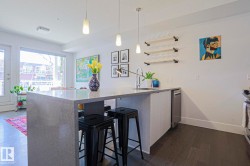 Open-concept kitchen featuring a waterfall island countertop, recessed sink with a high-arc faucet, stainless steel dishwasher, and wood-finish flooring - 