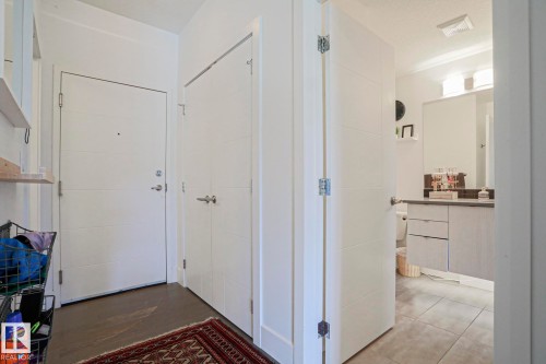 Foyer with panel doors, wood-finish flooring, and a powder room featuring a single vanity with a dark countertop and a wall-mounted light fixture - 202 10030 83 Avenue, Edmonton, AB - Indoor Photo Showing Other Room
