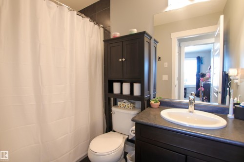 Bathroom featuring a dark wood-finish vanity with an integrated sink, a large wall-mounted mirror, and a toilet with an over-the-toilet storage cabinet - 3805 170A Avenue, Edmonton, AB - Indoor Photo Showing Bathroom