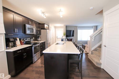 Kitchen featuring dark wood-finish cabinetry, stainless steel appliances, and light-toned countertops - 3805 170A Avenue, Edmonton, AB - Indoor Photo Showing Kitchen With Double Sink With Upgraded Kitchen