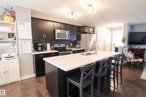 Open-concept kitchen featuring dark wood cabinetry, stainless steel appliances, and a large island with white countertops - 3805 170A Avenue, Edmonton, AB - Indoor Photo Showing Kitchen With Stainless Steel Kitchen With Double Sink