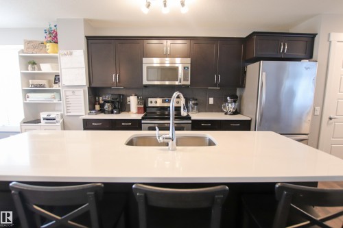 Kitchen featuring a spacious island with an undermount sink, dark wood-finish cabinetry, stainless steel appliances, and a tile backsplash - 3805 170A Avenue, Edmonton, AB - Indoor Photo Showing Kitchen With Stainless Steel Kitchen With Double Sink With Upgraded Kitchen