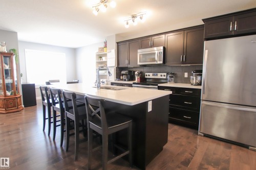 Modern kitchen featuring dark wood cabinetry, stainless steel appliances, and a central island with a light-toned countertop and integrated sink - 3805 170A Avenue, Edmonton, AB - Indoor Photo Showing Kitchen With Stainless Steel Kitchen With Upgraded Kitchen