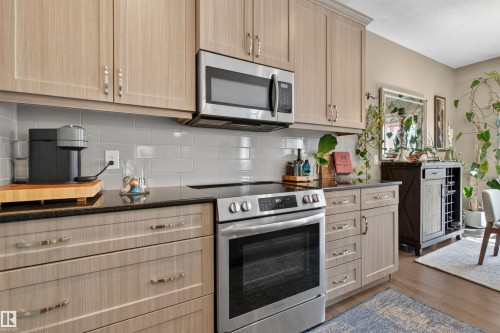 Modern kitchen featuring light wood-finish cabinetry, stainless steel appliances, a black countertop, and a light gray subway tile backsplash - 2313 Sparrow Crescent, Edmonton, AB - Indoor Photo Showing Kitchen