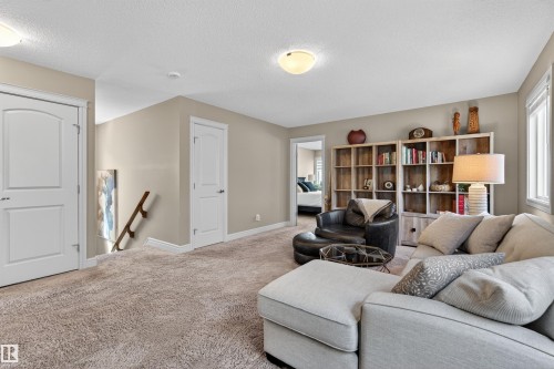 Carpeted upper-level space featuring light tan wall paint, multiple white paneled doors, and a built-in bookshelf unit - 2313 Sparrow Crescent, Edmonton, AB - Indoor Photo Showing Other Room