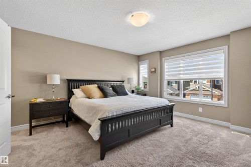Neutral-toned bedroom featuring plush carpet flooring, a large window with white blinds, and a white ceiling light fixture - 2313 Sparrow Crescent, Edmonton, AB - Indoor Photo Showing Bedroom