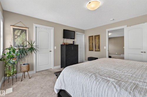 Spacious bedroom featuring light-toned walls, neutral carpet flooring, a large window, and two paneled interior doors with white trim - 2313 Sparrow Crescent, Edmonton, AB - Indoor Photo Showing Bedroom