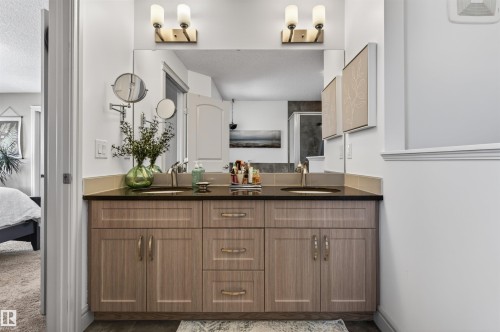 Double vanity featuring light wood-finish cabinetry, brushed nickel hardware, and dual undermount sinks with a dark countertop - 2313 Sparrow Crescent, Edmonton, AB - Indoor Photo Showing Bathroom