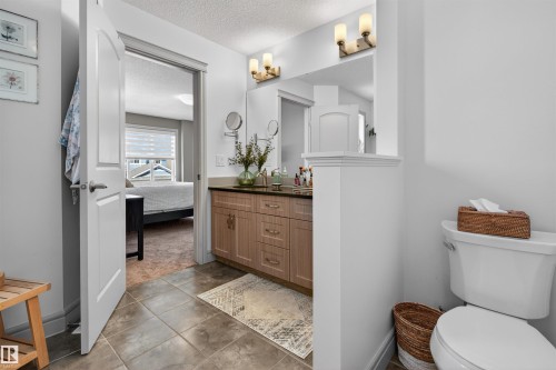 Bathroom featuring a wood-finish vanity with a dark countertop and integrated sink, dual wall-mounted vanity lights, ceramic tile flooring, and a toilet - 2313 Sparrow Crescent, Edmonton, AB - Indoor Photo Showing Bathroom