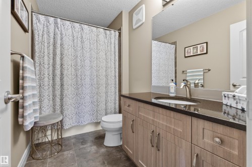 Full bathroom featuring a shower-tub combination, a vanity with an undermount sink and dark countertop, wood-finish cabinetry, and tile flooring - 2313 Sparrow Crescent, Edmonton, AB - Indoor Photo Showing Bathroom