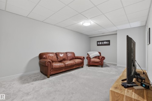 Spacious room featuring light gray carpeting, neutral wall finishes, and a grid panel ceiling with flush-mount lighting - 2313 Sparrow Crescent, Edmonton, AB - Indoor