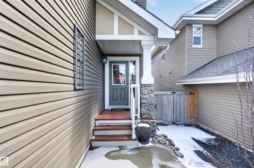 Covered entryway featuring a stone pillar accent, a dark green entry door with glass panes, white trim, and a wood-finish porch with stairs - 2313 Sparrow Crescent, Edmonton, AB - Outdoor With Exterior