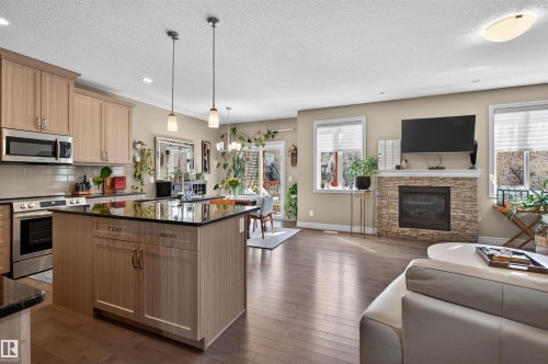 Open-concept living area featuring a kitchen with light wood-finish cabinetry, a large kitchen island with dark countertops, and stainless steel appliances - 2313 Sparrow Crescent, Edmonton, AB - Indoor Photo Showing Kitchen With Fireplace With Upgraded Kitchen