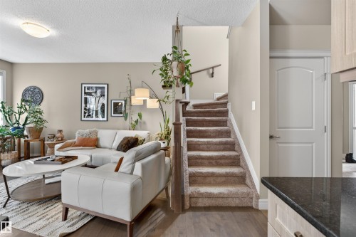 Open-concept living space featuring wood-finish flooring and a carpeted staircase with a wood handrail - 2313 Sparrow Crescent, Edmonton, AB - Indoor