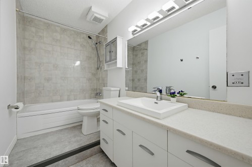Full bathroom featuring a rectangular vessel sink, white vanity with ample storage, large wall-mounted mirror, and a tub-shower combination with patterned tile surround - 8043 178 Street, Edmonton, AB - Indoor Photo Showing Bathroom