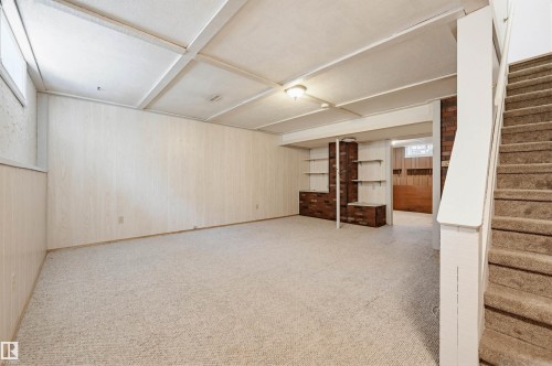 Carpeted recreation room featuring paneling walls, a tiled drop ceiling, and a built-in brick shelving unit with open shelves - 8043 178 Street, Edmonton, AB - Indoor Photo Showing Other Room