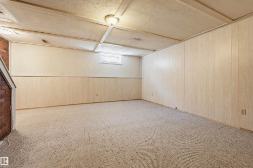 Spacious room featuring light-toned paneling, a drop ceiling with integrated lighting, and a brick-finish architectural element - 8043 178 Street, Edmonton, AB - Indoor Photo Showing Other Room