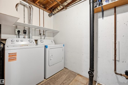 Dedicated utility area featuring a washer and dryer, convenient overhead shelving, exposed ceiling joists, and visible copper plumbing - 8043 178 Street, Edmonton, AB - Indoor Photo Showing Laundry Room