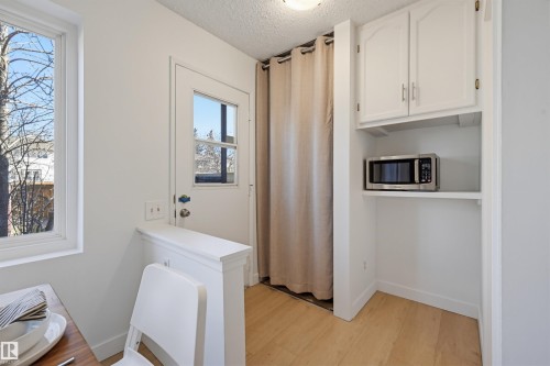 Compact kitchen nook featuring white cabinetry, a built-in microwave shelf, and wood-finish flooring - 8043 178 Street, Edmonton, AB - Indoor Photo Showing Other Room