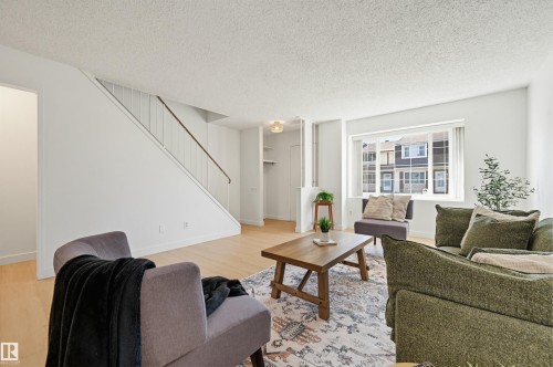 Bright living area featuring wood-finish flooring, a contemporary staircase with white risers and a dark handrail, a large window with horizontal blinds, and a built-in shelving unit - 8043 178 Street, Edmonton, AB - Indoor Photo Showing Living Room